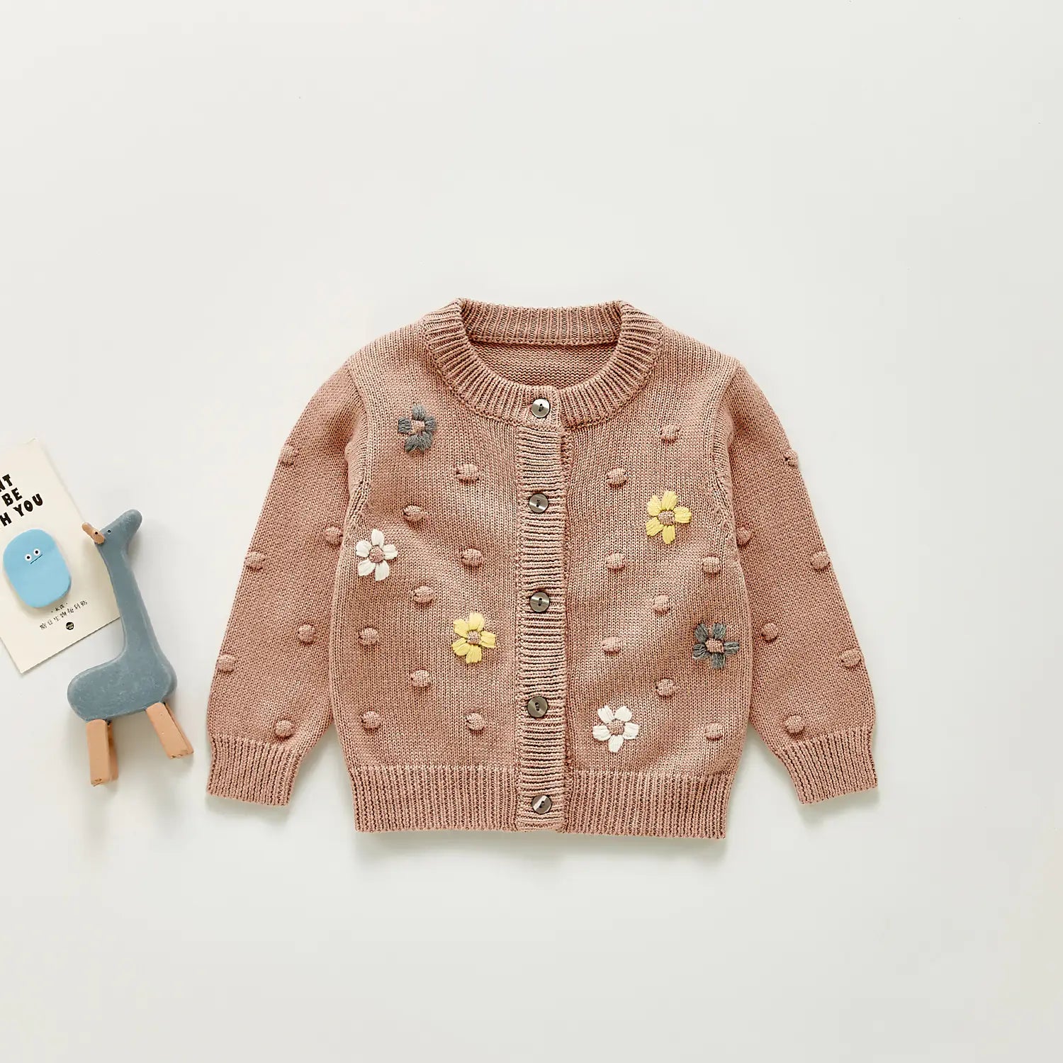 Children's dusty pink cardigan with floral embellishments on a light grey background