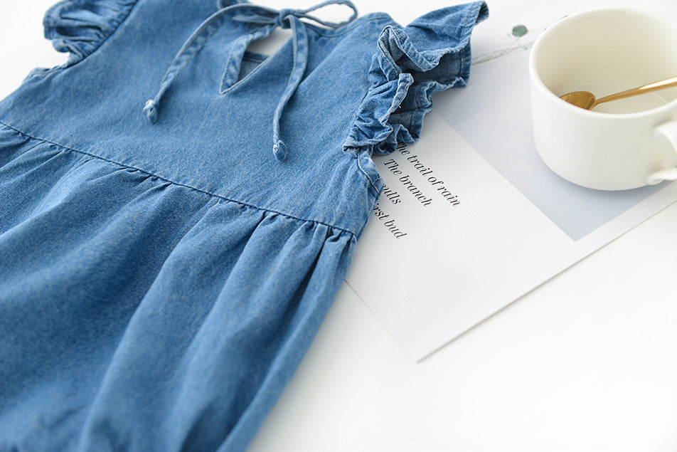 Blue girls denim dress on a white surface with a cup and spoon.