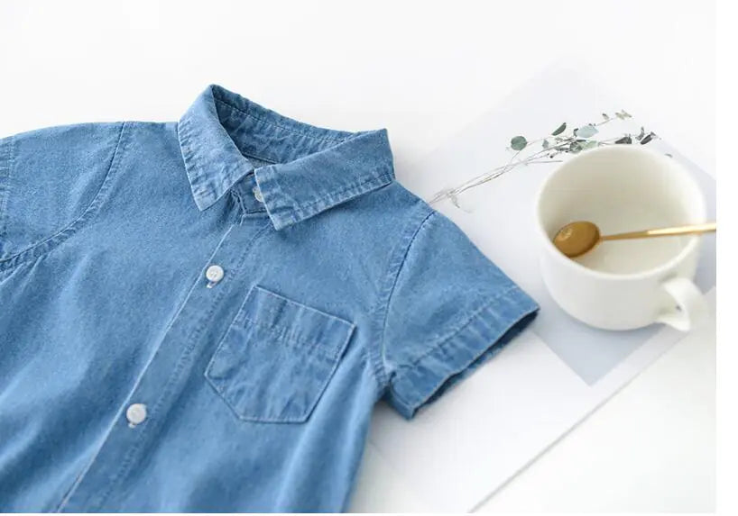 Blue boys denim shirt on a white surface with a cup and spoon.