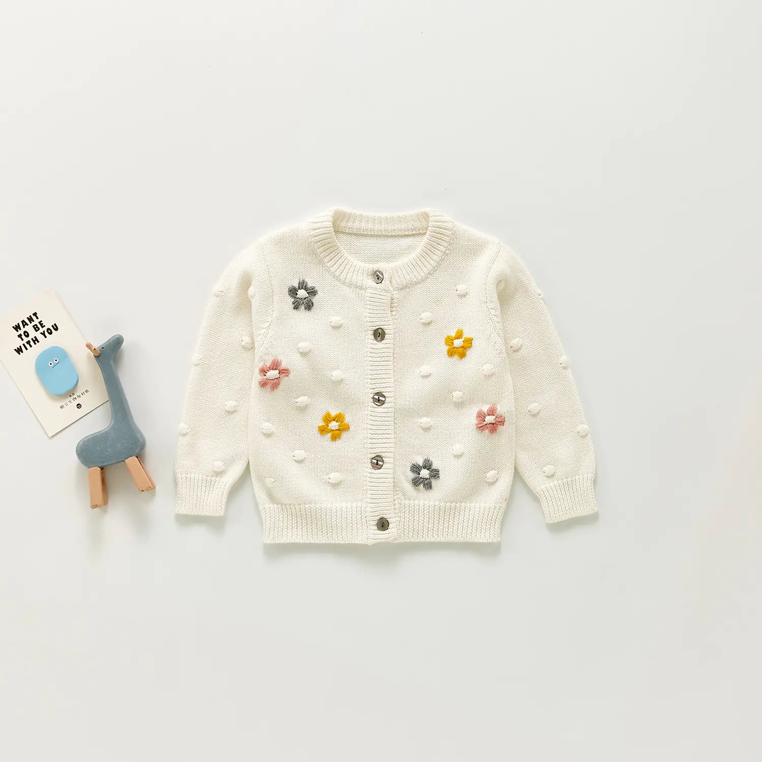Children's white cardigan with floral embellishments on a light grey background