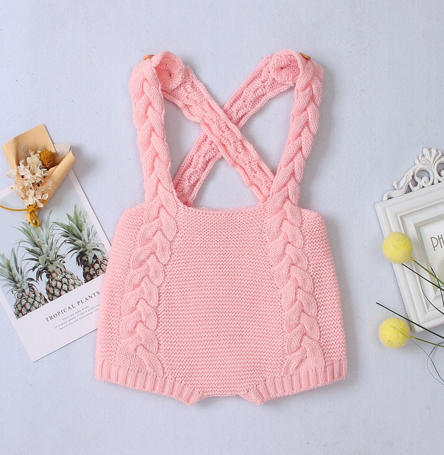 Pink knitted romper with criss-cross straps on a light gray background
