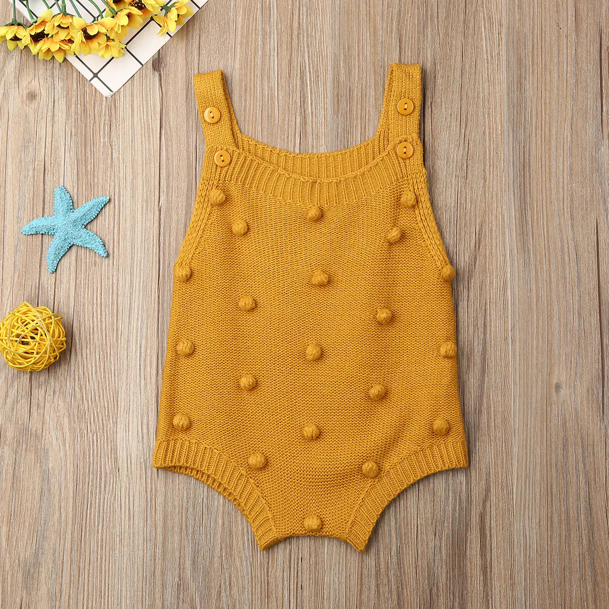 Mustard knitted romper with button details on a gray background