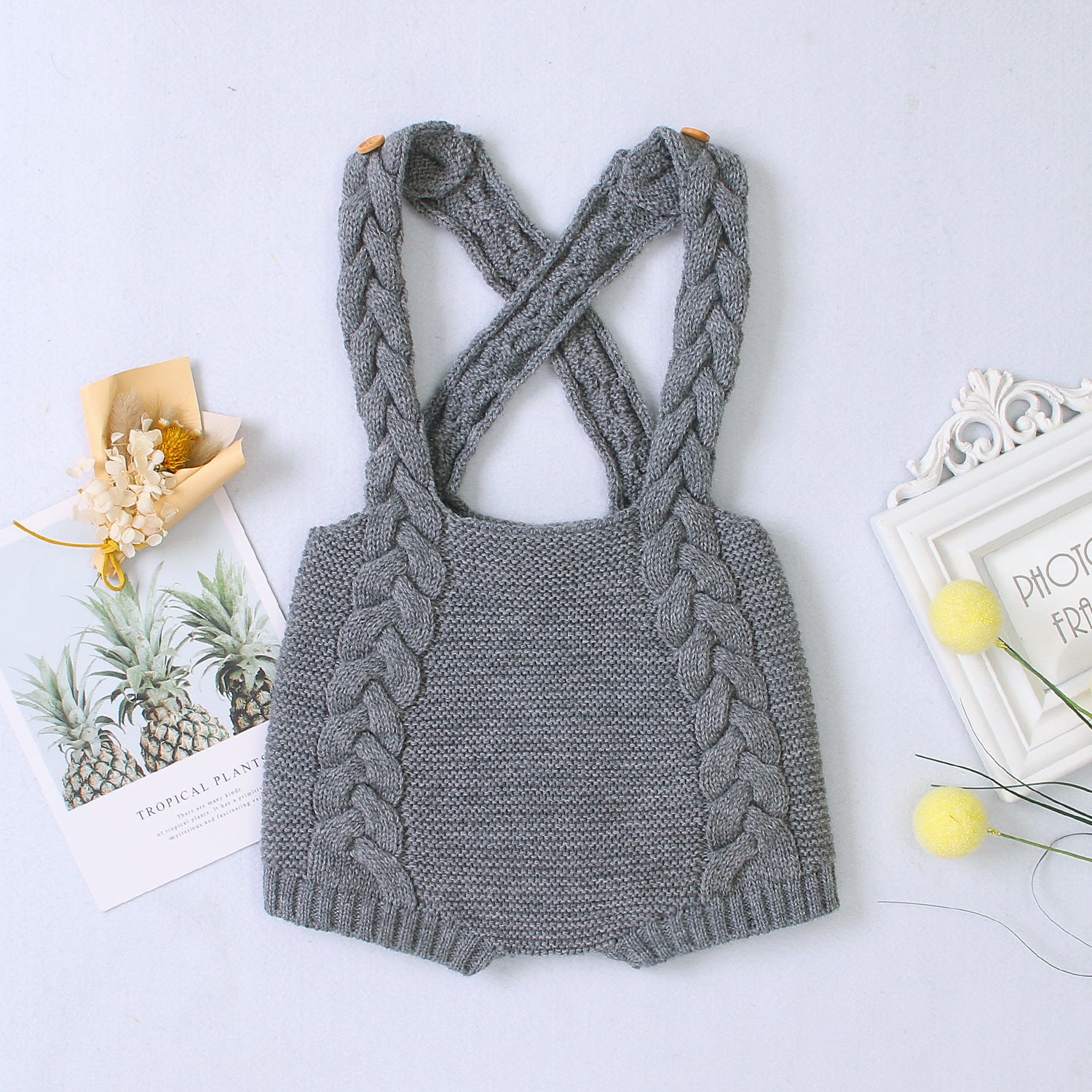 Dark grey knitted romper with braided straps on a light gray background