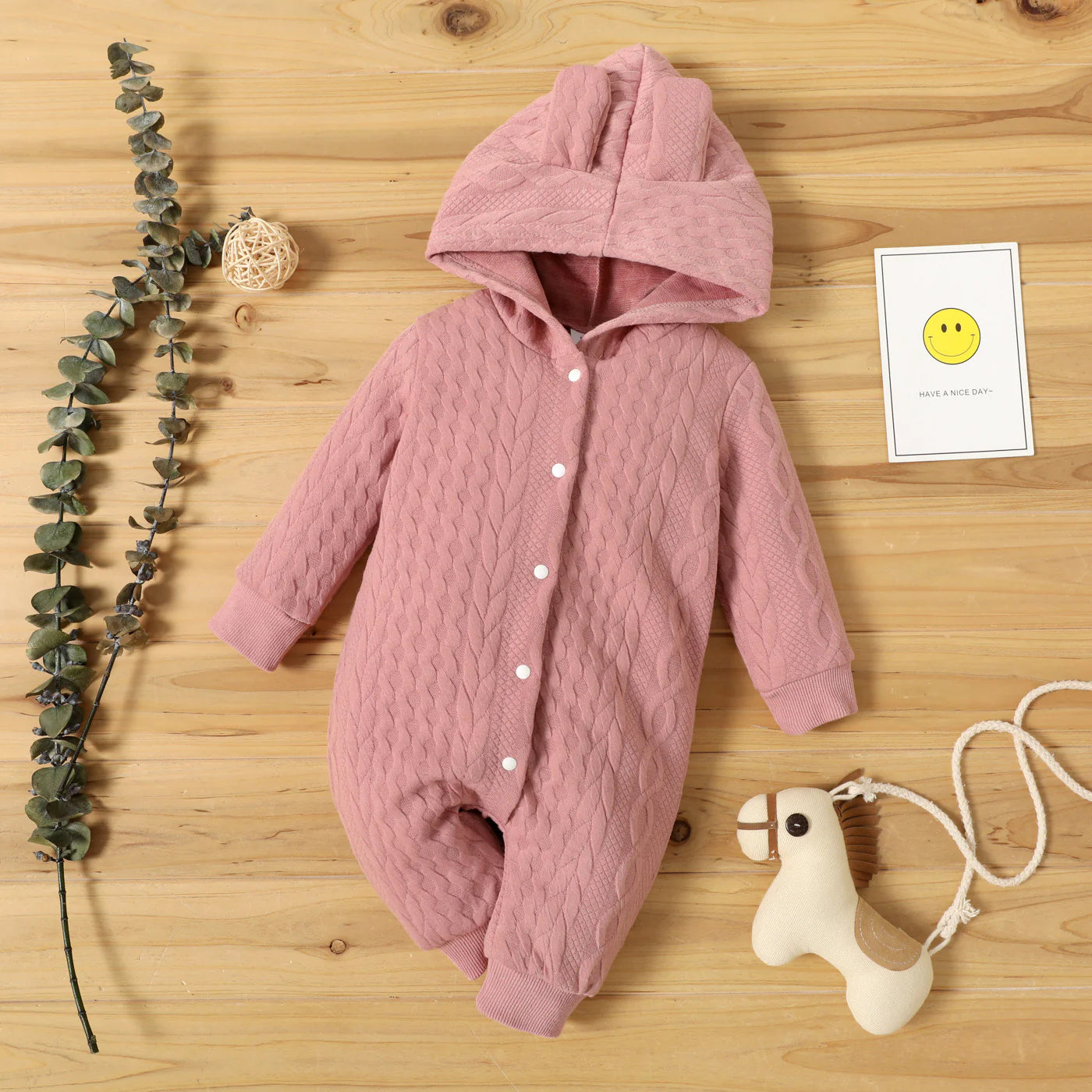 Pink baby onesie with buttons on a wooden surface with decorative elements.