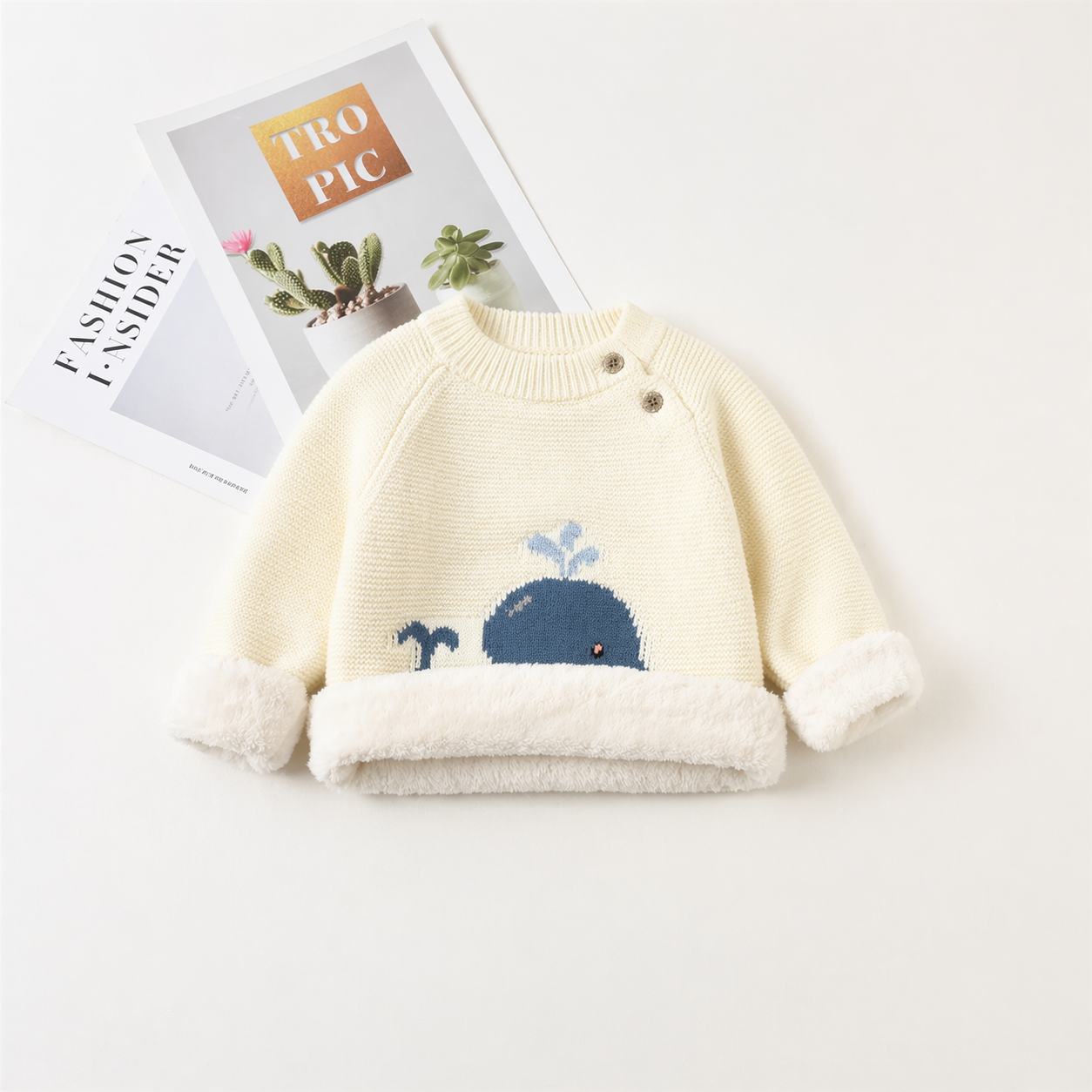 Baby ivory white sweater with whale design on a white surface