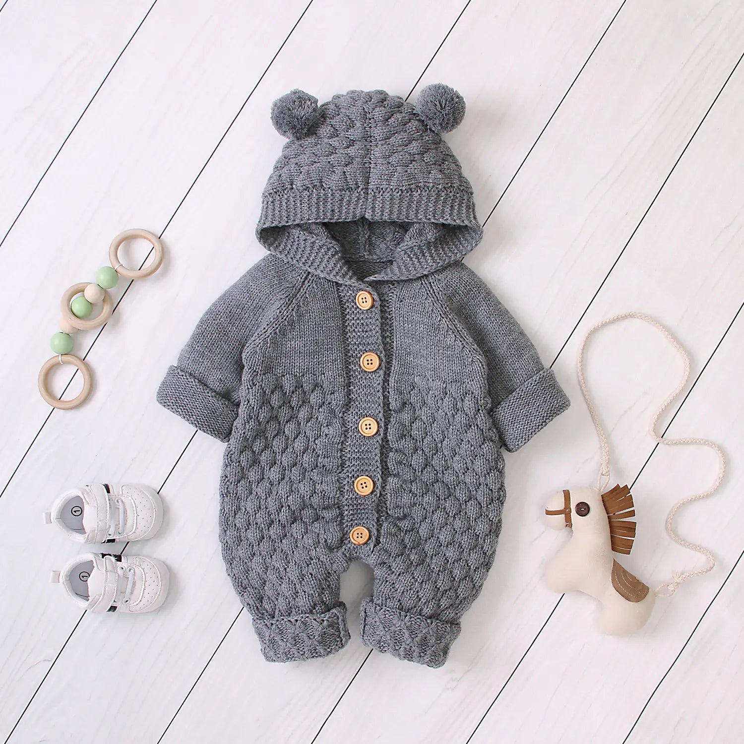 Grey knitted baby romper with bear ears on a white wooden floor.