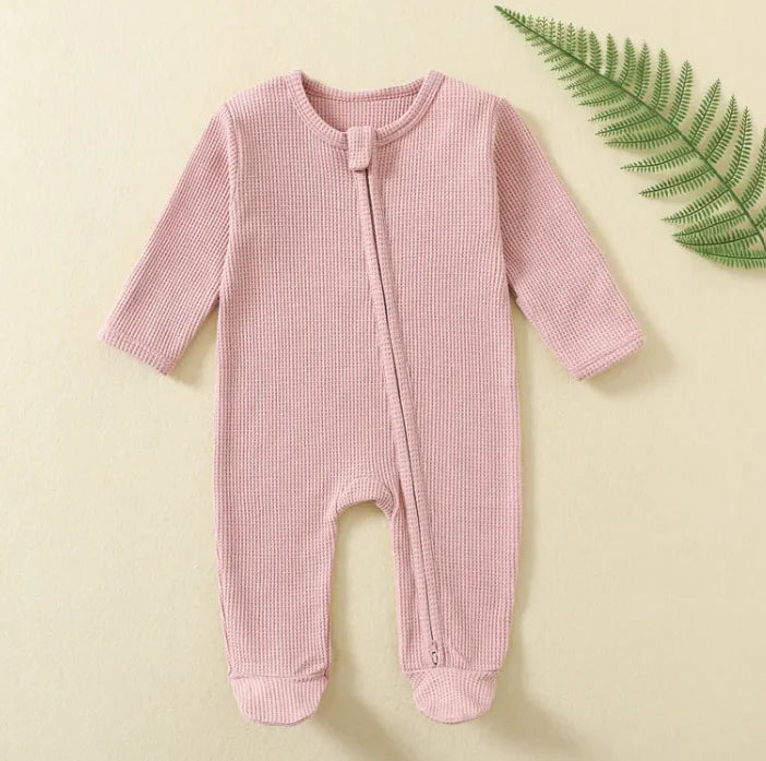 Pink baby onesie on a beige background with a green leaf