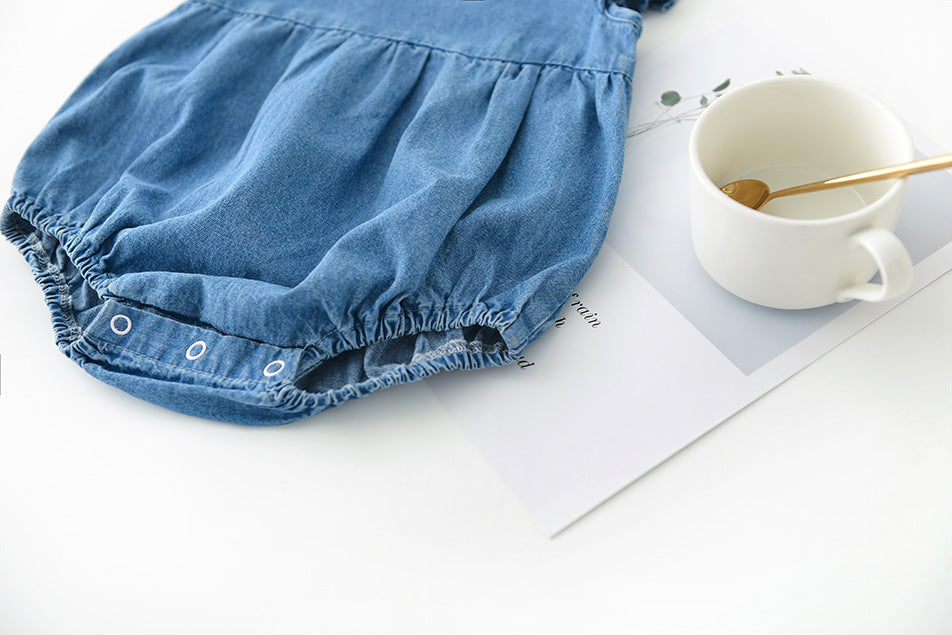 Blue girls denim baby romper on a white surface with a mug and spoon.