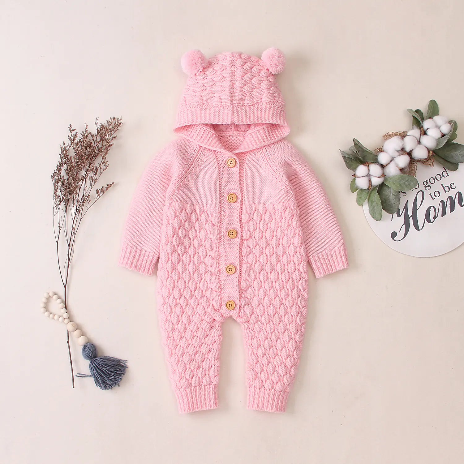 Light pink knitted baby romper with hood on a light beige background