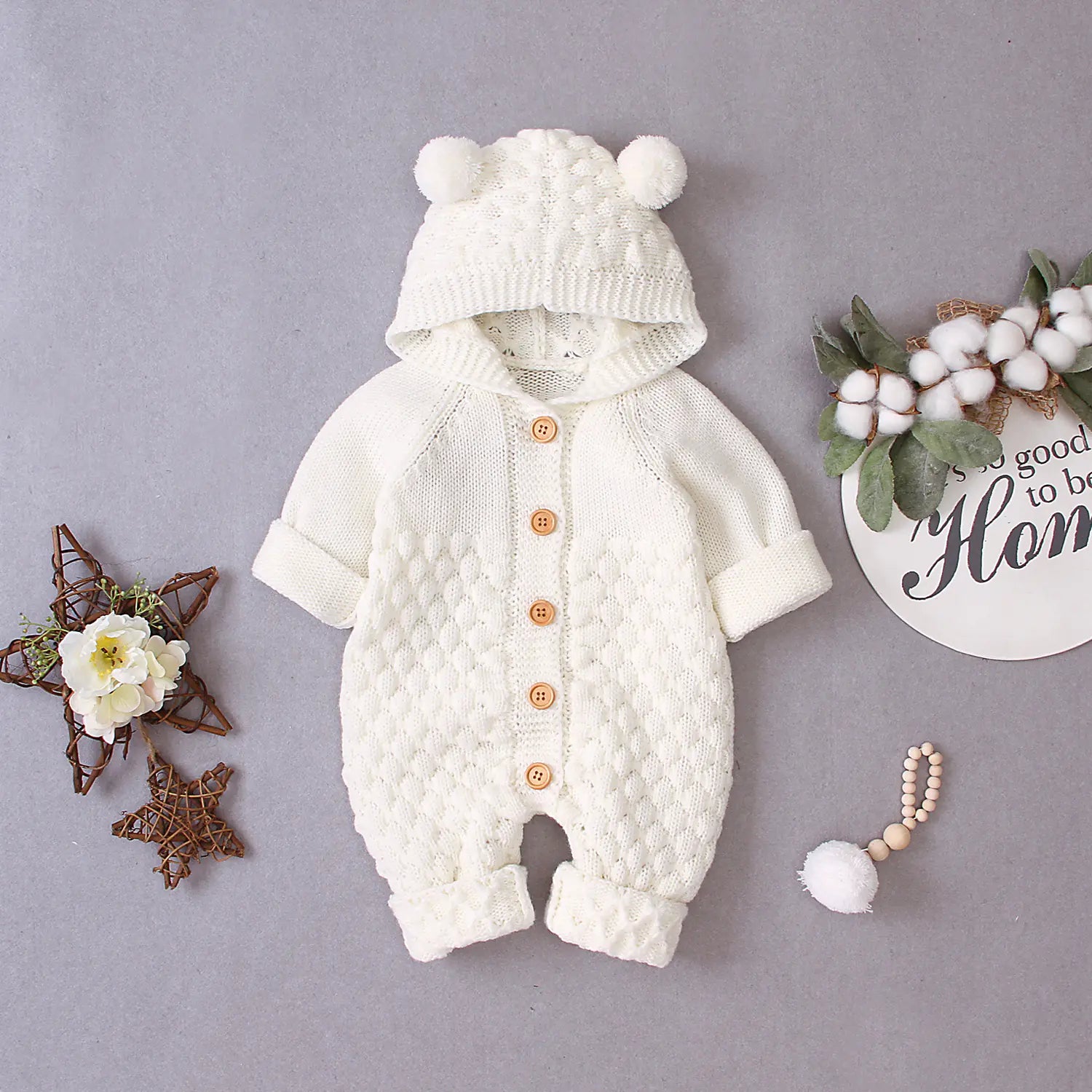 Beige knitted baby romper with pom-pom details on a gray background