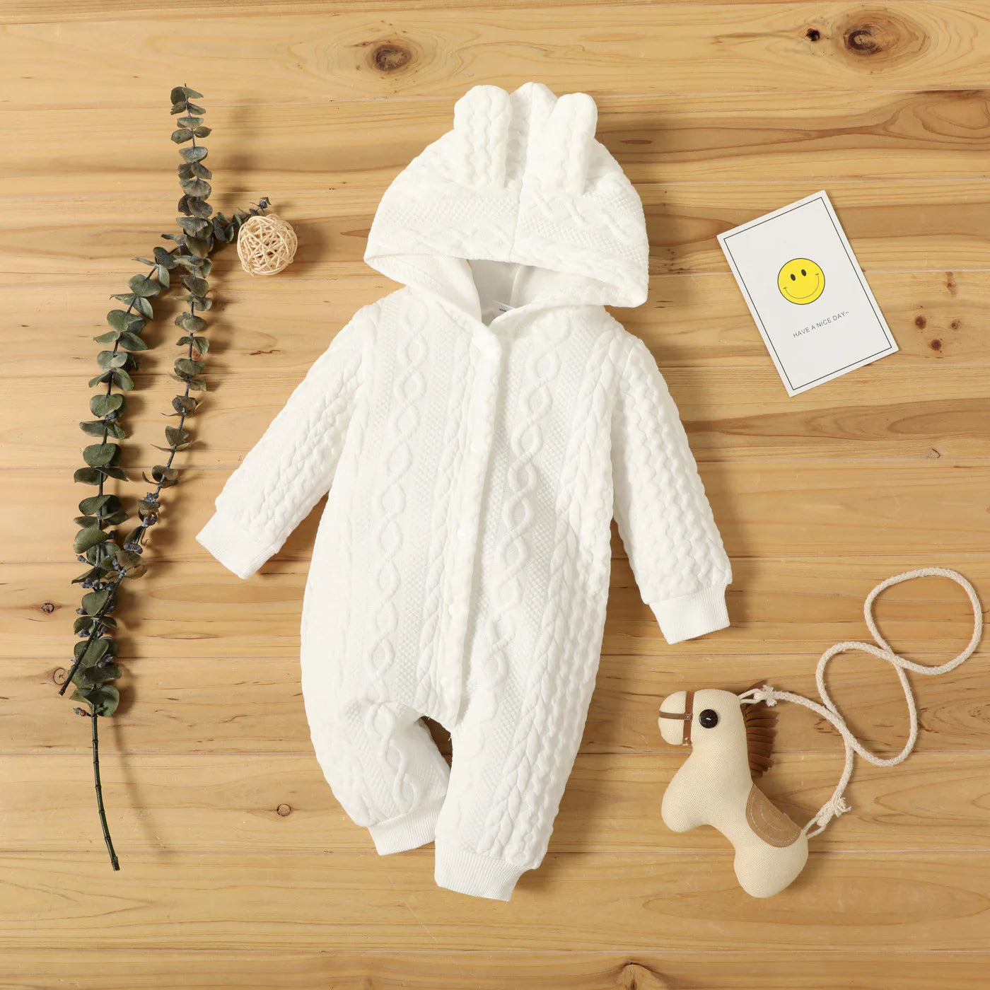 White baby snowsuit with cable knit pattern on a wooden surface with decorative elements.