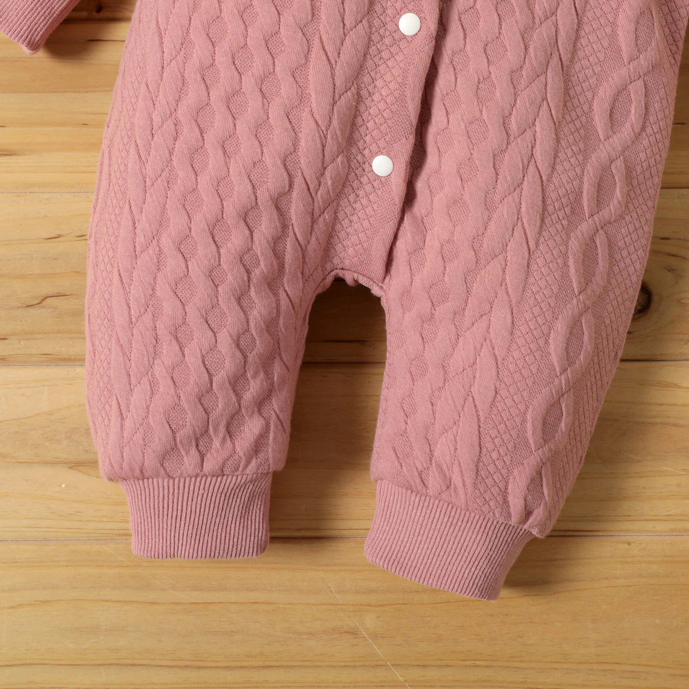 Pink baby romper with buttons on a wooden surface 