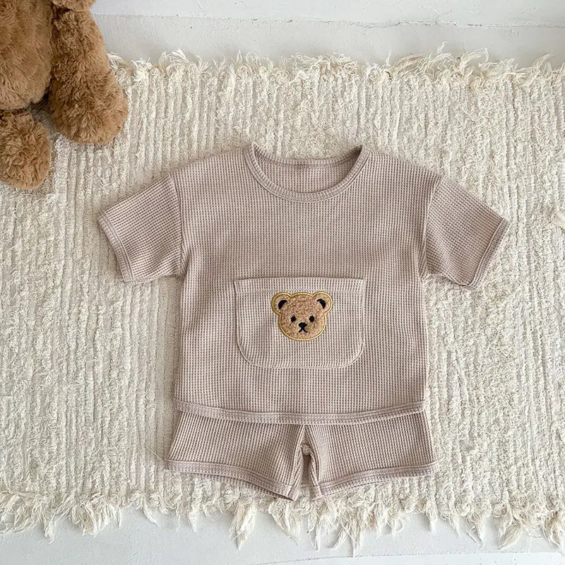 Children's taupe outfit with teddy bear design on a textured white surface