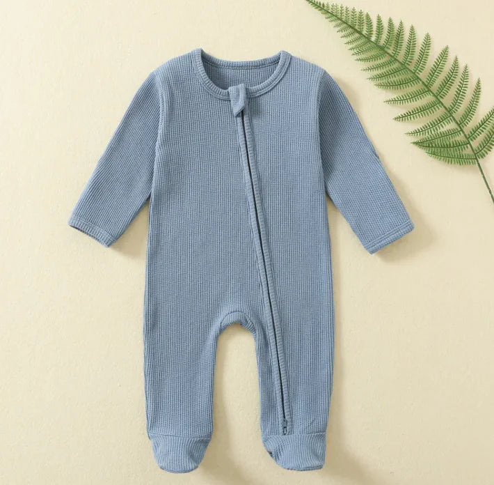 Blue baby onesie on a beige background with a green leaf