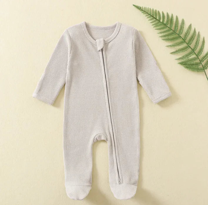 Light grey baby onesie with a zipper on a beige background with a green leaf